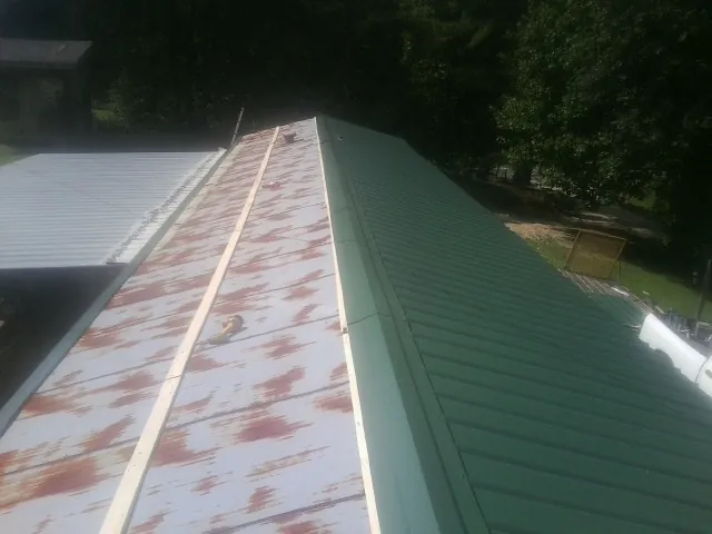 Old rusted panels beside newly installed green metal roofing — Wind Damage Roof Repair by Roofing Brothers in Maplewood