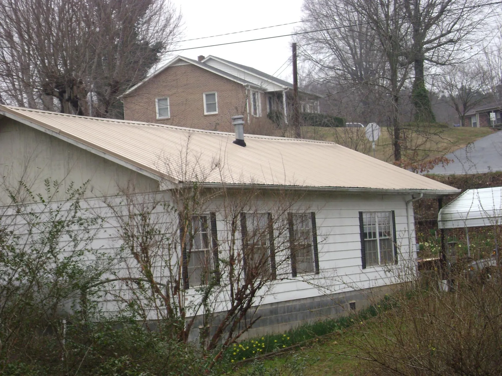 Tan metal roof on a white sided house set into a hillside — Commercial Roofing by Roofing Brothers in Maplewood